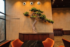 A reception desk with a bonsai tree, a wooden bench, and orange chairs.