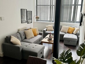 A modern living room with two grey sofas, a coffee table, and a large window with blinds. - Mathew Street CITY - City 1 BDR apt sleeps 6 (Merseyside)