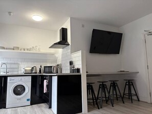 A compact kitchen with a washing machine, a microwave, and a toaster. There are stools at the bar area. - Jude`s Place 2 - 1 bed apt sleeps 4 (Merseyside)