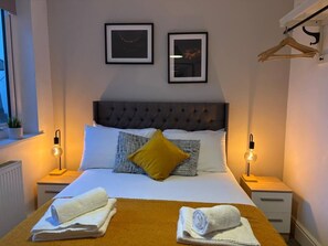 Een netjes opgemaakt bed met hoofdeinde, twee bedlampen en een raam met een plant.