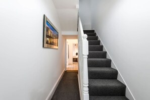 A hallway with a carpeted staircase, a framed picture on the wall, and a welcome mat at the bottom. - Jude`s Place 2 - 1 bed apt sleeps 4 (Merseyside)