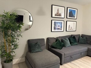 A living room with a grey sofa set, a round mirror, and framed pictures on the wall. - Jude`s Place 2 - 1 bed apt sleeps 4 (Merseyside)