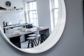 A modern kitchen with a central island, bar stools, and a view through a circular mirror. - Jude`s Place 3- 1 bed apt/ 1 sofabed sleeps 4 (Merseyside)