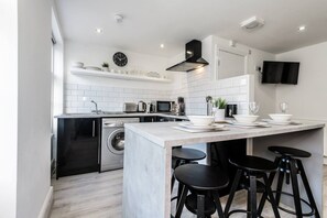 A modern kitchen with a central island, bar stools, a washing machine, and a flat-screen TV mounted on the wall. - Jude`s Place 3- 1 bed apt/ 1 sofabed sleeps 4 (Merseyside)