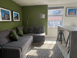 A living room with a sectional sofa, a desk with two stools, a floor lamp, and framed pictures on the walls. - Jude`s Place 3- 1 bed apt/ 1 sofabed sleeps 4 (Merseyside)