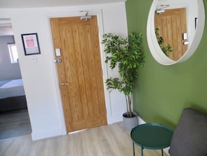 A room with a wooden door, a potted plant, a green chair, and a round mirror on the wall. - Jude`s Place 3- 1 bed apt/ 1 sofabed sleeps 4 (Merseyside)