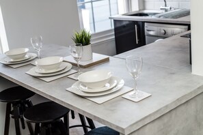 A modern kitchen with a marble countertop, white plates, bowls, and wine glasses set for a meal. - Jude`s Place 3- 1 bed apt/ 1 sofabed sleeps 4 (Merseyside)