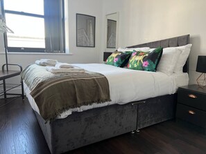A modern bedroom with a large bed, a bedside table, a lamp, and artwork on the walls. - Mathew Street - City 1 BDR apt sleeps 6 (Merseyside)
