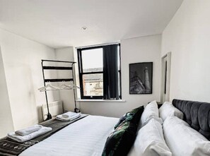 A hotel room with a bed, a window with curtains, a radiator, a towel rack, and a framed picture on the wall. - Mathew Street - City 1 BDR apt sleeps 6 (Merseyside)