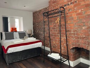 Ein Schlafzimmer mit einer Ziegelwand, einem Bett mit rotem und weißem Überwurf, einem schwarzen Metalltrockner und einem Kamin.