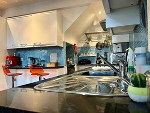 A modern kitchen with a central island, a sink, and a dining area with orange chairs. - Boss Places converted warehouse-Mathew St. 2 bed (Merseyside)