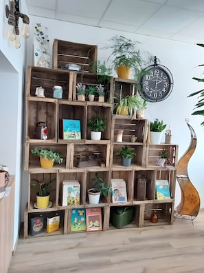 Una estantería de madera con varios niveles que contiene libros, plantas en macetas y objetos decorativos.