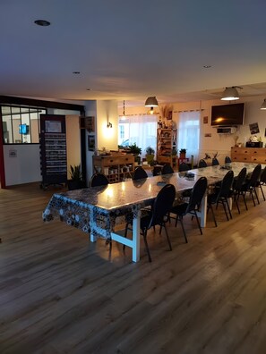A spacious dining area with a long table, chairs, and a kitchen in the background. - Bed and Breakfast 'Chambre 1' with Shared Terrace, Wi-Fi and Air Conditioning (Saint-Gervais)