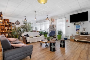 A spacious living room with a sofa, armchair, and a coffee table. There are multiple potted plants and a hanging chair. - Bed and Breakfast 'Chambre 5' with Shared Terrace, Wi-Fi and Air Conditioning (Saint-Gervais)