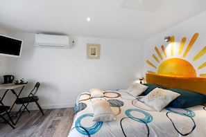 A hotel room with a bed, a desk with a chair, a flat-screen TV, an air conditioning unit, and a wall-mounted artwork. - Bed and Breakfast 'Chambre 5' with Shared Terrace, Wi-Fi and Air Conditioning (Saint-Gervais)