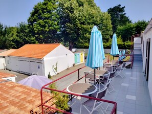 Eine Terrasse mit Sitzgelegenheiten, ein weißes Gebäude mit rotem Dach und einem blauen Sonnenschirm.