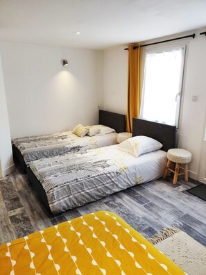 Ein Doppelbett mit gemusterten Betttextilien, ein Holzschemel und ein Fenster mit Vorhängen.