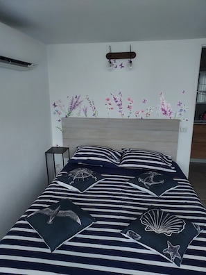 Una cama con ropa de cama a rayas y almohadas decorativas, una mesita de noche y una pared con adhesivos florales.