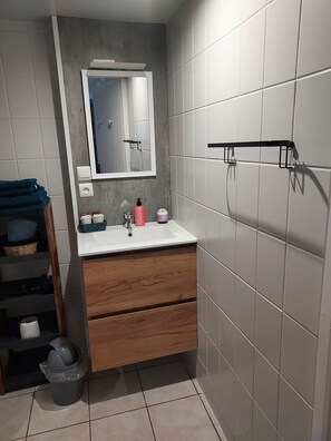 Ein Badezimmer mit weißem Waschbecken, Holzschrank, Spiegel und gefliesten Wänden.