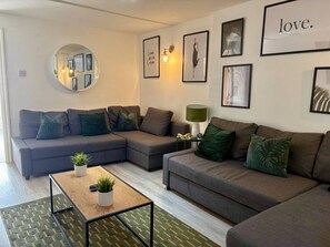 A living room with a sectional sofa, a coffee table, and a mirror on the wall. - Jude`s Place 1 - 2 bedroomed apt/ 2 sofabeds (Merseyside)