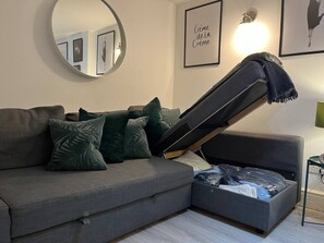A modern living room with a sofa, a coffee table, a round mirror, and a wall-mounted light fixture. - Jude`s Place 1 - 2 bedroomed apt/ 2 sofabeds (Merseyside)