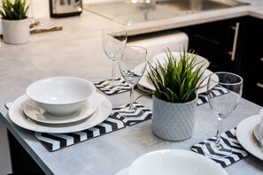 A modern kitchen with a marble countertop, white plates, bowls, and glassware arranged for dining. - Jude`s Place 1 - 2 bedroomed apt/ 2 sofabeds (Merseyside)