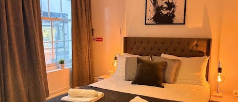 A hotel room with a bed, two bedside tables, a window with curtains, a wall-mounted artwork, and a 'No entry' sign.