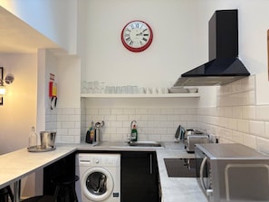 Eine kleine Küche mit Waschmaschine, Spüle, Herd und einer Uhr an der Wand.