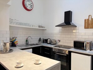 Eine moderne Küche mit weißen Fliesen, Edelstahlgeräten, einer schwarzen Dunstabzugshaube und einer Uhr an der Wand.