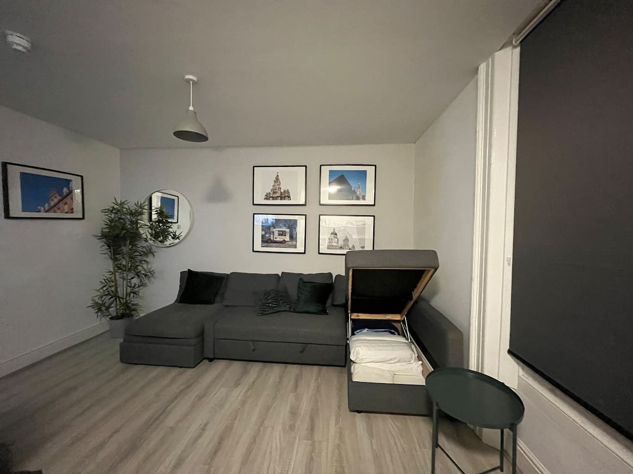 A modern living room with a sectional sofa, a small table, a chair, a large mirror, and framed pictures on the wall.