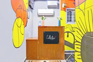 A reception desk with a sign, a wall-mounted air conditioner, and a window with a view. - Collection O De Alphabet Hotel UMCC (Hyderabad)