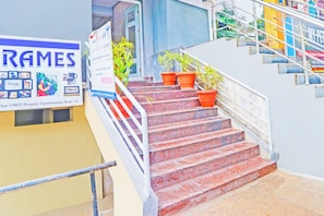 A staircase with red steps leading to a landing, flanked by potted plants and a signboard. - Collection O De Alphabet Hotel UMCC (Hyderabad)