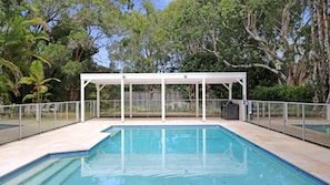 A rectangular swimming pool with a white covered seating area in the background. - Beaches Apartment 13 – Bennett’s Beach Retreat (Hawks Nest)