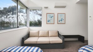 A room with a cushioned bench, a sofa with cushions, and two framed floral artworks on the wall. - Beaches Apartment 13 – Bennett’s Beach Retreat (Hawks Nest)