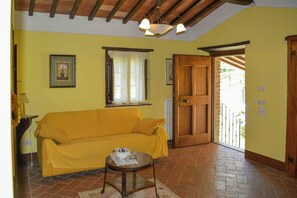 Une pièce avec un canapé jaune, une petite table ronde sur laquelle se trouve un objet blanc, une porte en bois et une fenêtre avec des rideaux.
