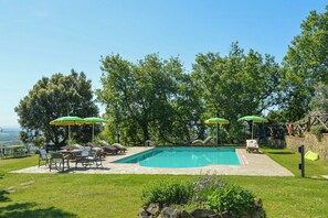 A swimming pool with lounge chairs and umbrellas, surrounded by trees and a stone wall. - Villa on organic farm between Chianti and Arezzo (Civitella In Val di Chiana)