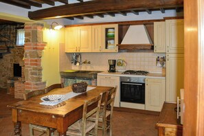 A rustic kitchen with a wooden table, chairs, a stove, and a brick wall. - Villa on organic farm between Chianti and Arezzo (Civitella In Val di Chiana)