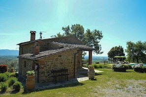 A stone building with a sloped roof, a bench, and a view of the landscape. - Villa on organic farm between Chianti and Arezzo (Civitella In Val di Chiana)