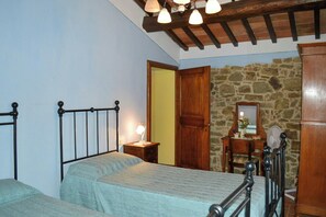 A bedroom with a bed, bedside table, lamp, wooden wardrobe, and a stone wall. - Villa on organic farm between Chianti and Arezzo (Civitella In Val di Chiana)