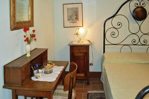 Une chambre à coucher avec un lit, une commode en bois, un bureau avec une lampe, une chaise et une petite table avec un panier.