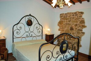 Une chambre à coucher avec un lit en métal, un mur en pierre et un lustre.