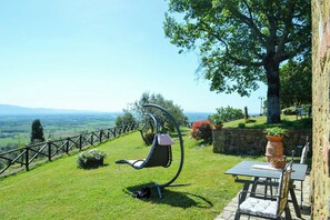 A garden with a swing chair, a stone wall, and a table with chairs. - Villa on organic farm between Chianti and Arezzo (Civitella In Val di Chiana)