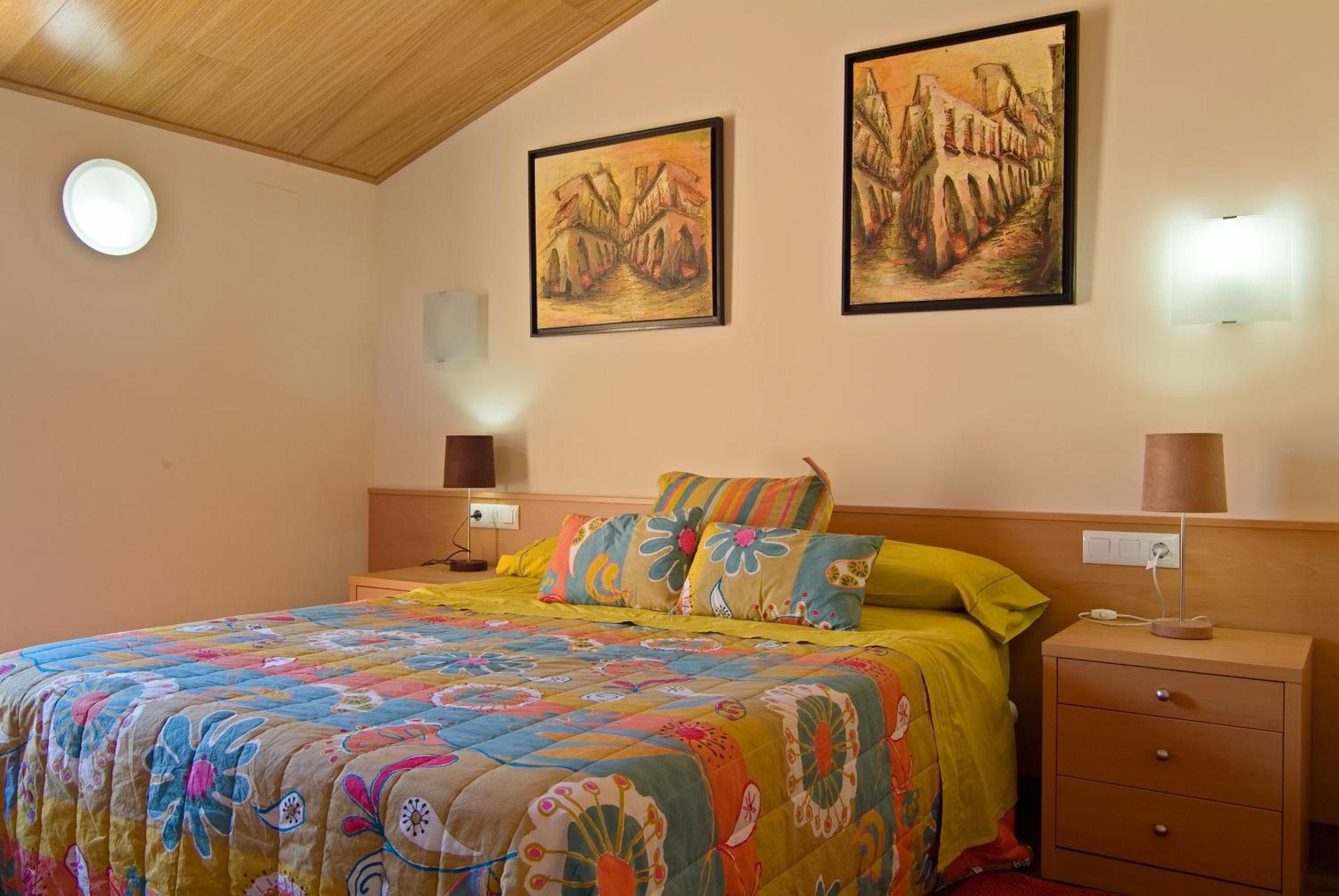 Een slaapkamer met een bed, twee bedlampen, een nachtkastje en twee aan de muur hangende schilderijen.