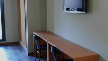Una habitación con una mesa de madera larga, dos sillas, un televisor montado en la pared y una puerta.