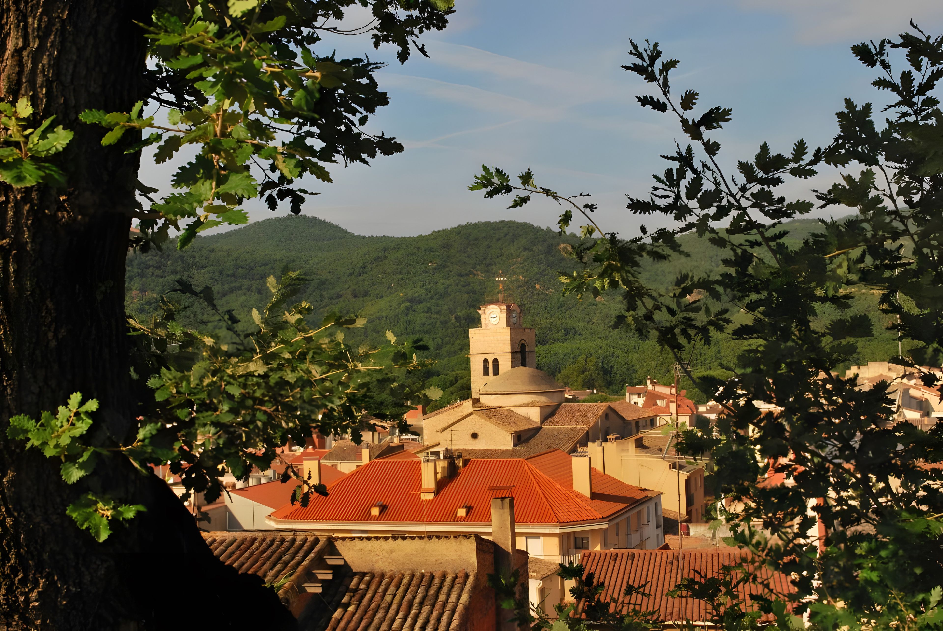 Uma cidade com uma igreja imponente e um campanário, cercada por vegetação e colinas.