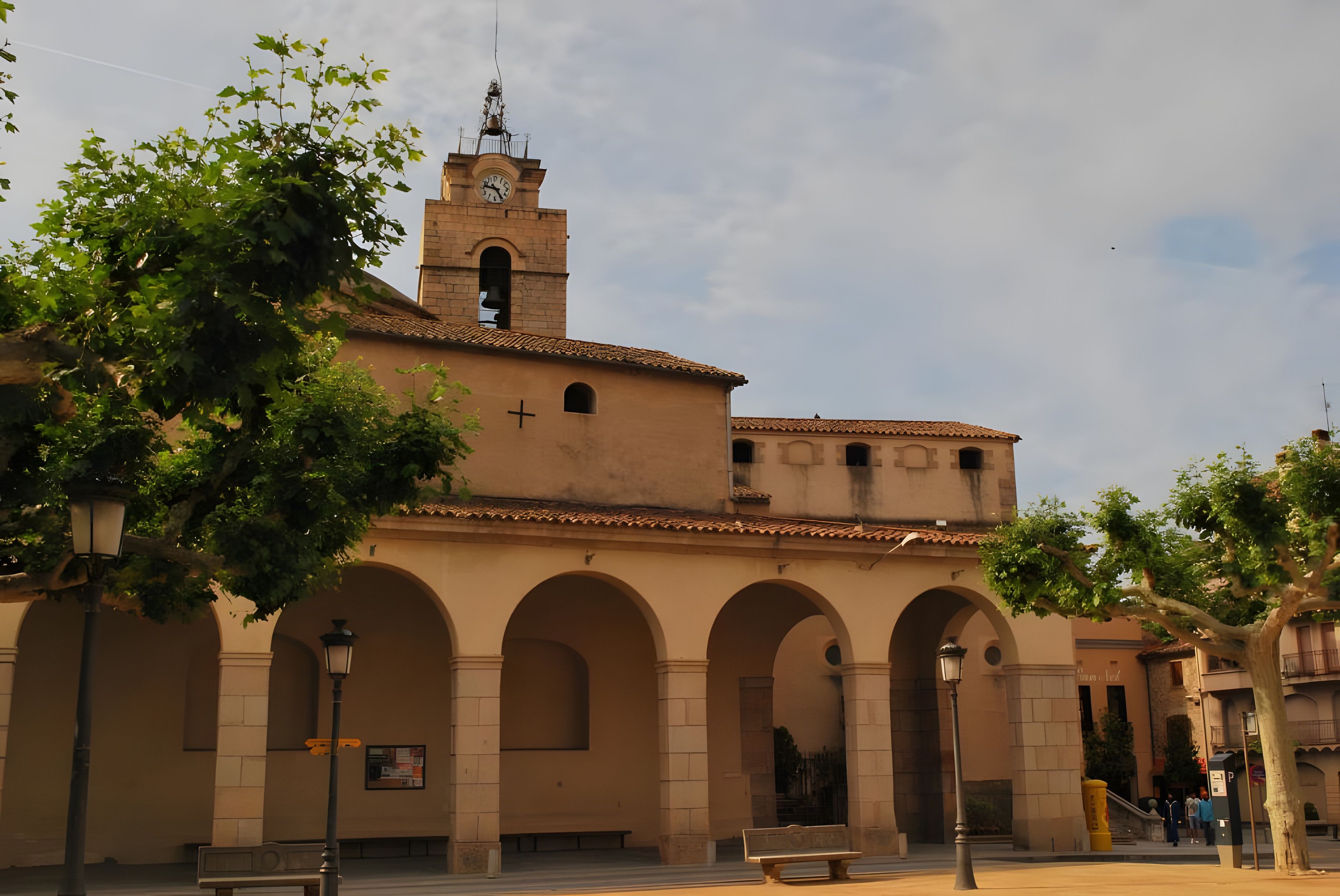 Un edificio histórico con una torre de reloj, paseos en arco y una cruz en la fachada.