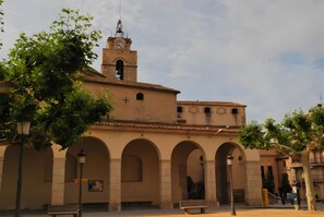 Ein historisches Gebäude mit einem Glockenturm, Bogenarkaden und einem Kreuz an der Fassade.