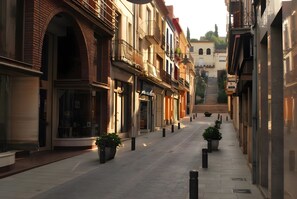 A narrow street with buildings on either side, featuring balconies and storefronts.