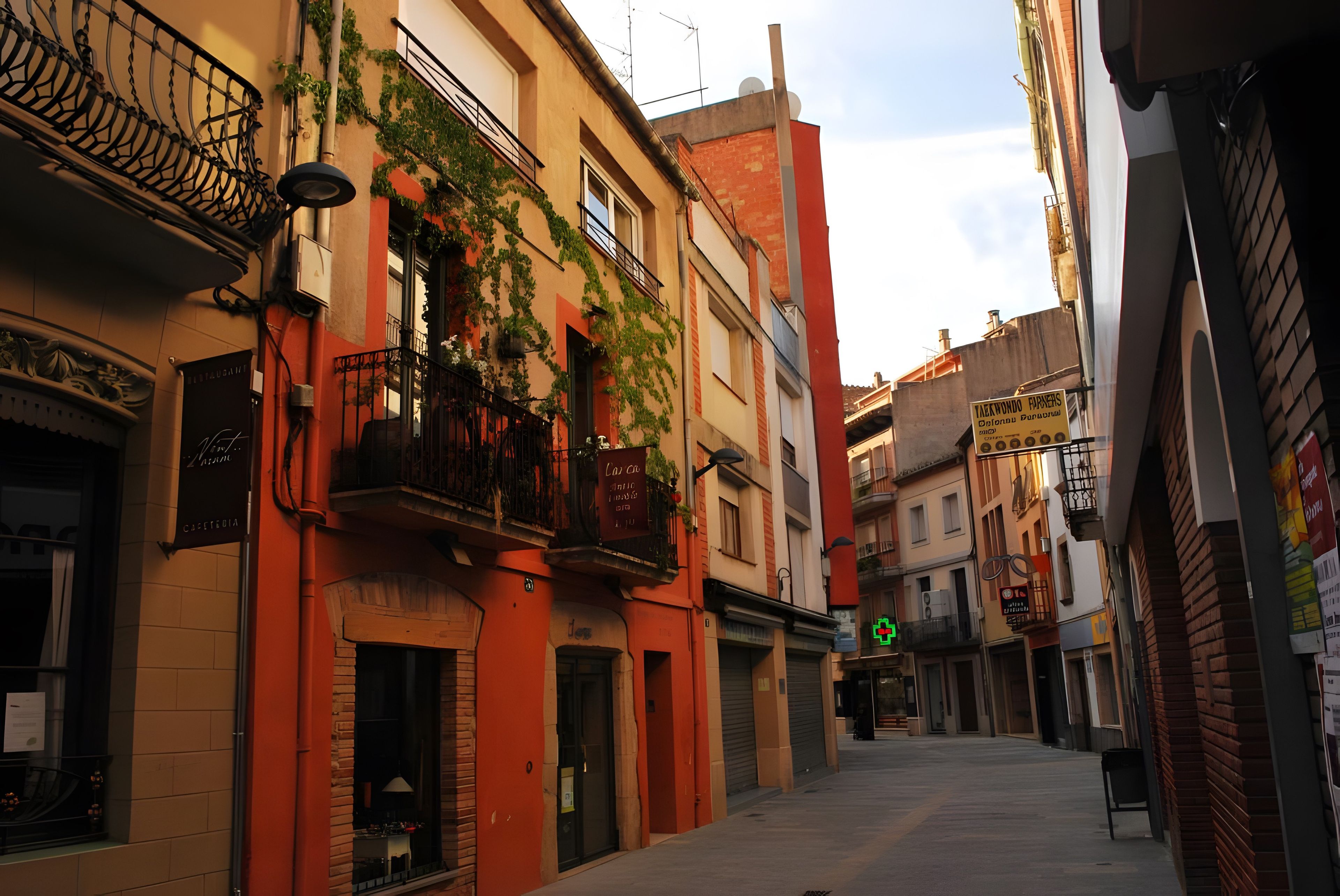 A narrow street with buildings featuring balconies and signage.