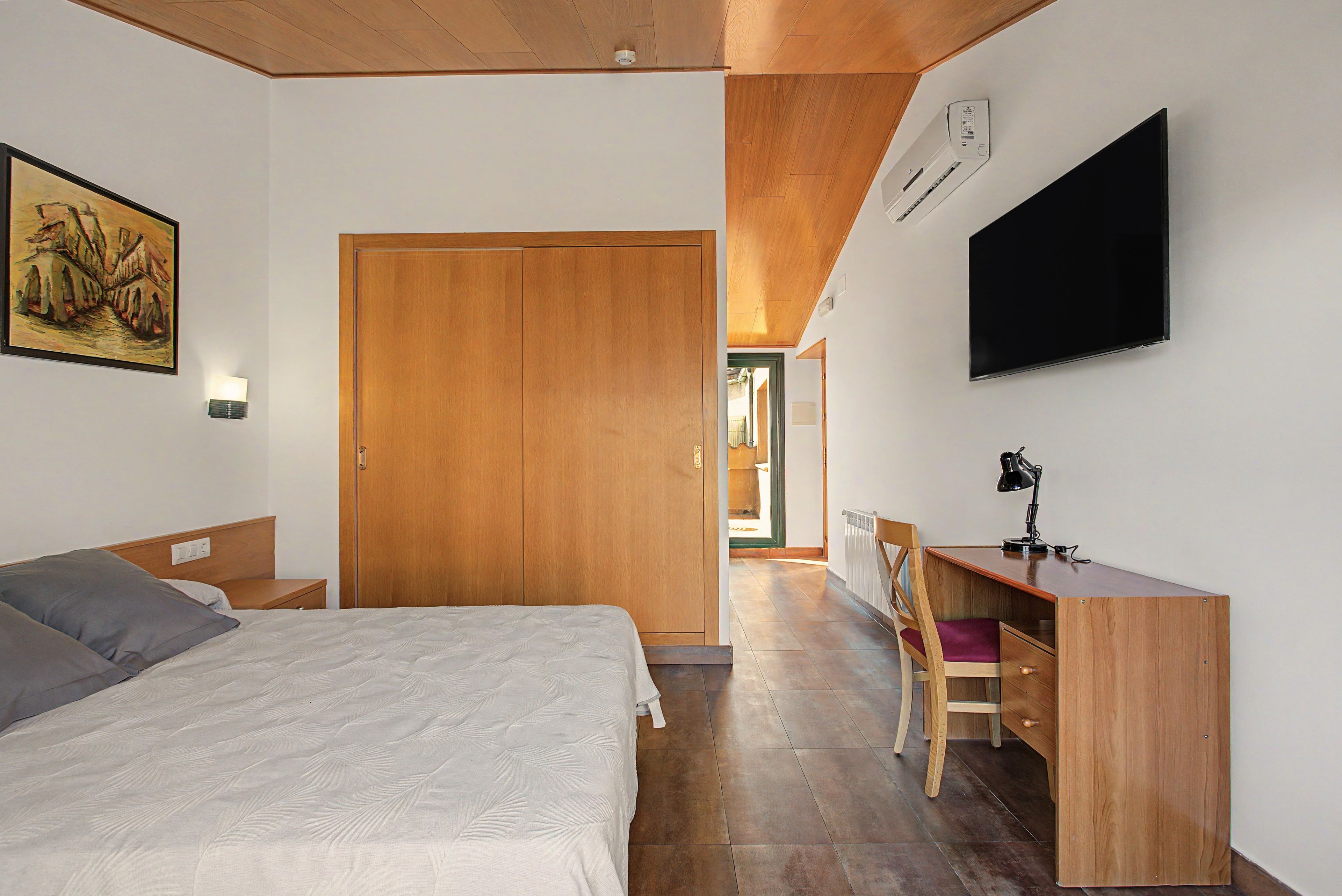 Un dormitorio con una cama, un escritorio, una silla, un televisor y un armario.